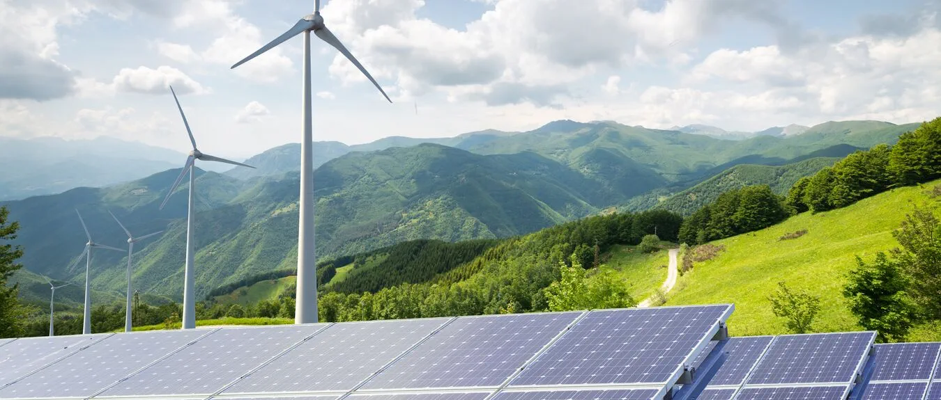 solar panels with wind turbines against mountanis landscape against blue sky with clouds